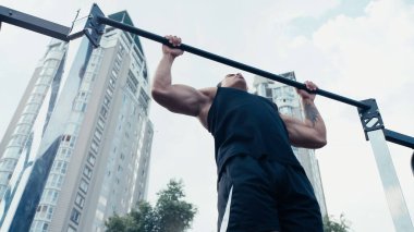 Açık havada yatay barda sportif karışık ırk eğitiminin düşük açılı görüntüsü
