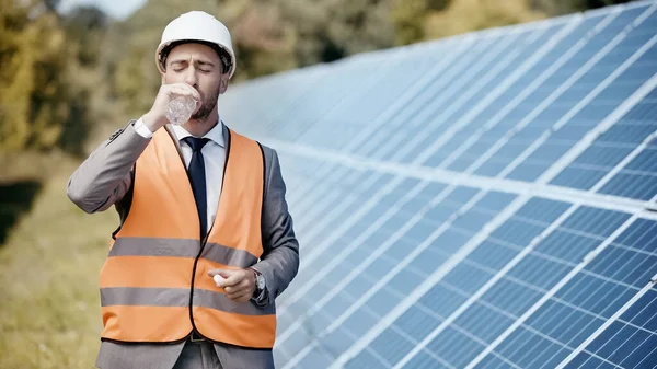 Geschäftsmann Warnweste Trinkt Wasser Der Nähe Von Sonnenkollektoren — Stockfoto