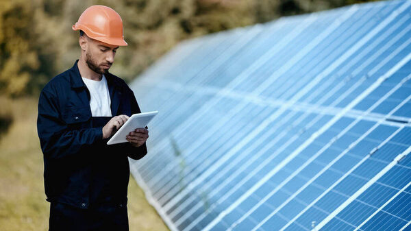 engineer using gadget while standing near solar panel 