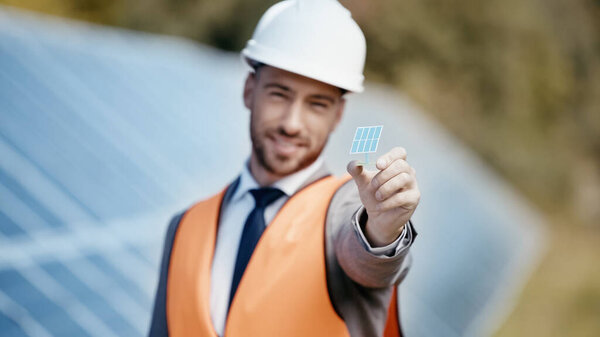 blurred and smiling businessman showing small solar battery model