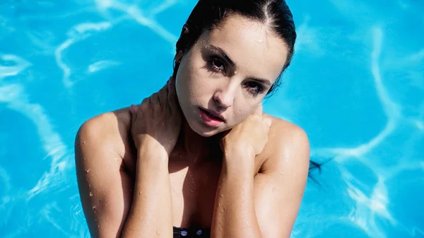 brunette woman with wet hair swimming in pool with blue water