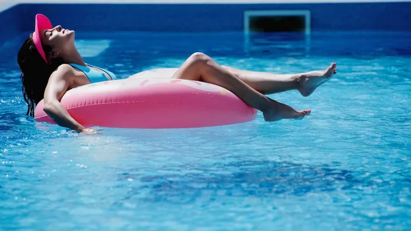 cheerful woman with closed eyes swimming on swim ring in pool