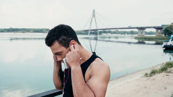 Athletic Racial Man Adjusting Earphones While Standing River — Stock Photo, Image