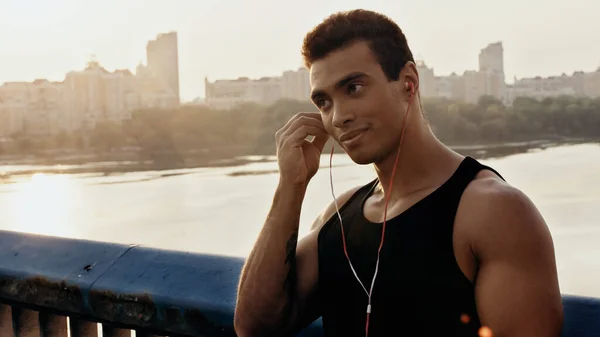 Athletic Racial Man Adjusting Earphones While Standing Bridge River — Stock Photo, Image