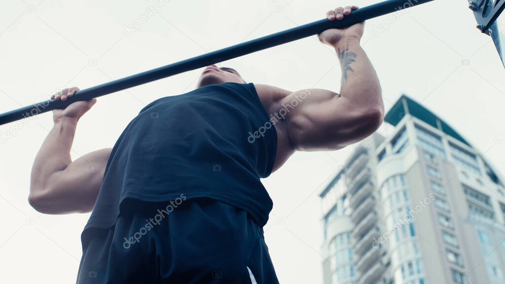 low angle view of athletic bi-racial man training on horizontal bar outdoors