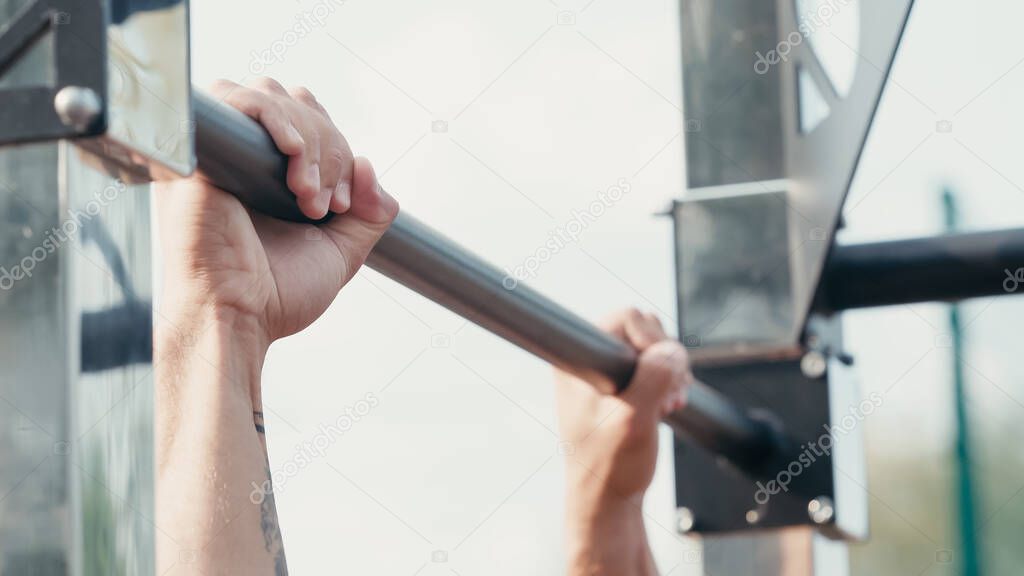 cropped view of sportsman working out on horizontal bar outdoors