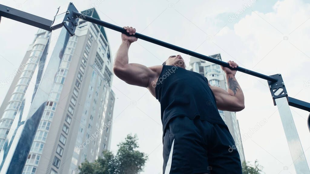 low angle view of sportive mixed race man training on horizontal bar outdoors