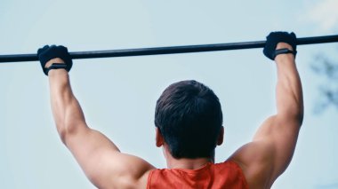 Genç sporcunun arka görüntüsü yatay çubukta barfiks çekerken.