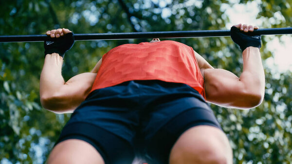 bottom view of young sportsman doing pull ups on horizontal bar outside