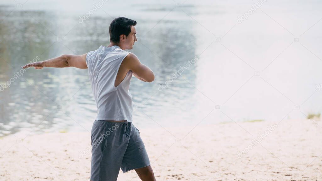 side view of athletic young sportsman warming up near river