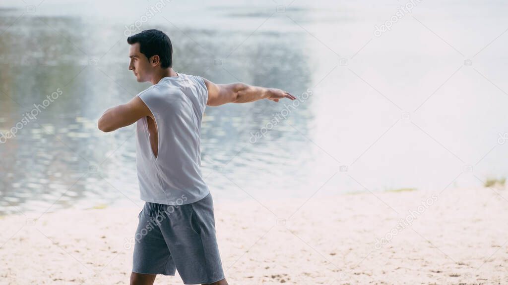 side view of young sportsman warming up while doing body rotation near river