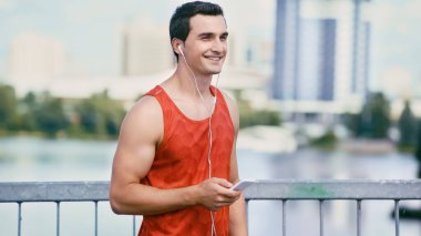 Akıllı telefonu tutan ve kulaklıkla müzik dinleyen mutlu sporcu.