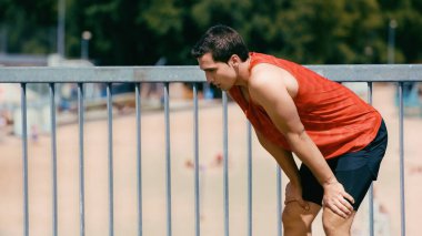 young sportsman breathing while resting after jogging on bridge clipart