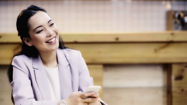 kafede akıllı telefon kullanarak takım elbise li gülümseyen ve oldukça Asyalı iş kadını 