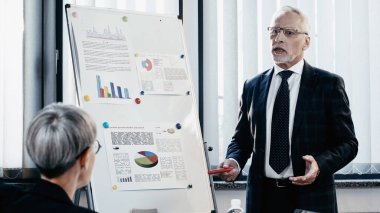 Resmi giyinen olgun bir işadamı yakın çalışma çizelgesi ve ofis arkadaşı konuşuyor. 
