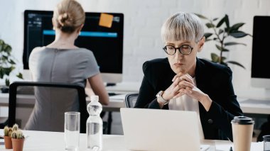 Resmi görevdeki düşünceli iş kadını ofisteki içkilerin yanındaki laptopa bakıyor. 