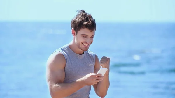 Deportista Excitado Usando Teléfono Móvil Cerca Del Mar Borroso — Foto de Stock