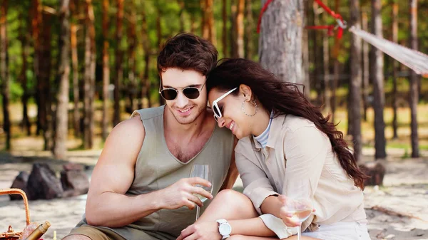 笑顔男でサングラスを持っているガラスのワイン近くのガールフレンドとピクニックバスケットオンビーチ — ストック写真