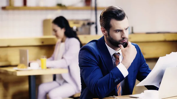 Pensiv Affärsman Tittar Dokument Nära Bärbar Dator Och Suddig Kvinna — Stockfoto