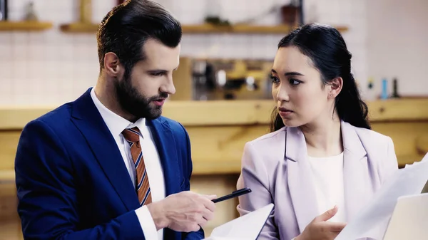 Brodaty Biznesmen Trzymający Notatnik Długopis Pobliżu Azjatyckiej Bizneswoman Dokumentami Kawiarni — Zdjęcie stockowe