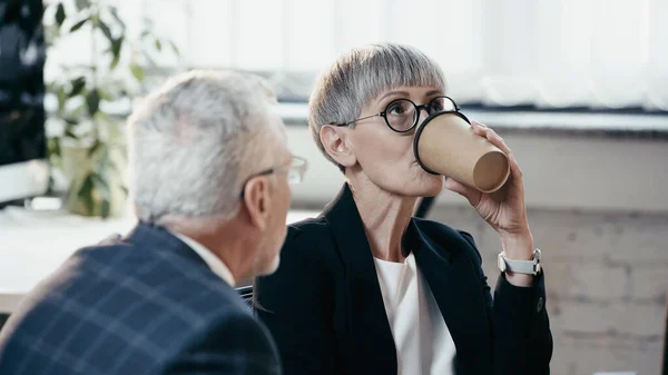 Mature Businesswoman Drinking Coffee Blurred Colleague Office — Stock Photo, Image
