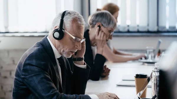 Mature Businessman Headset Eyeglasses Using Laptop Blurred Colleagues — Stock Photo, Image