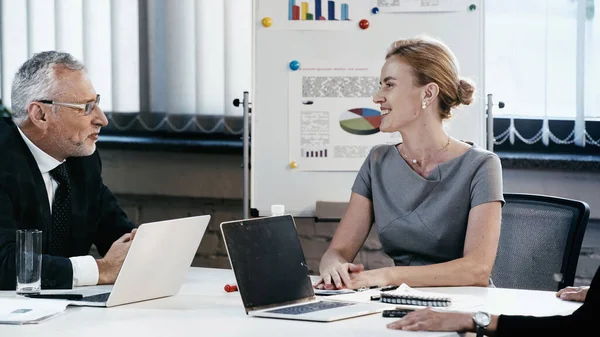 Mujer Negocios Sonriente Hablando Con Colega Cerca Computadoras Portátiles Durante — Foto de Stock