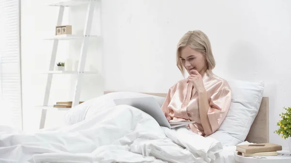 Glimlachende Blonde Freelancer Met Behulp Van Laptop Terwijl Zitten Bed — Stockfoto