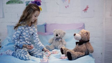 Pijamalı çocuk, oyuncakların yanında çay fincanlarıyla oynuyor. 