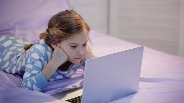 Girl in pajama watching cartoons on laptop in bedroom in evening  clipart