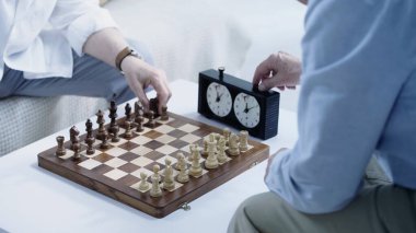 partial view of senior man using timer while playing chess with friend