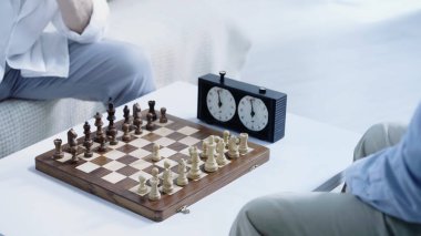 chessboard with figures near timer and cropped senior men