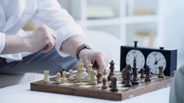 cropped view of senior man moving chess figure while gaming at home