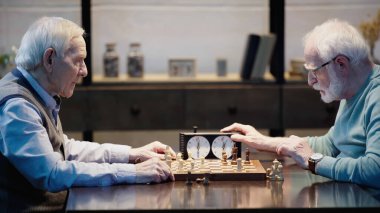 side view of man fixing time on chess clock while playing with friend at home 