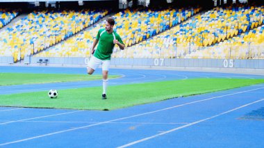 full length of young and bearded football player in uniform warming up at stadium 
