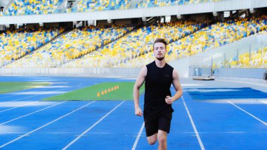 bearded and sportive man in dark sportswear running at stadium 