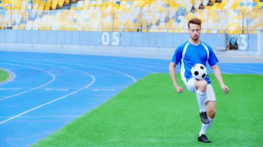 young football player bouncing soccer ball with legs on stadium 