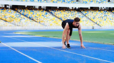 bearded man in sportswear standing at starting pose before running at stadium 