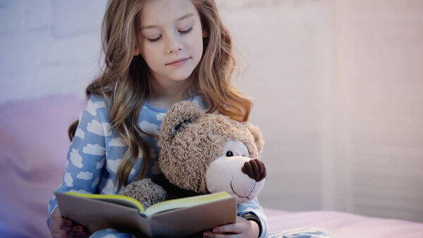 Preteen kid holding soft toy while reading book in bedroom 
