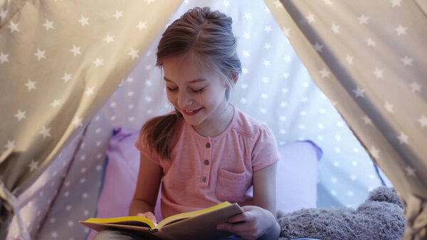 Happy preteen kid reading book in wigwam at home 