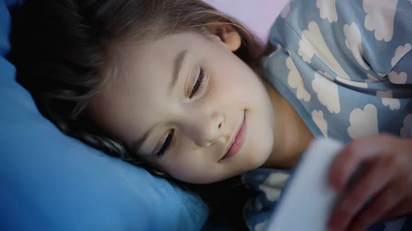 Mosolygó Kiskorú Gyermek Néz Elmosódott Okostelefon Ágyban — Stock Fotó