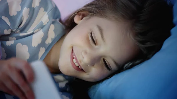 Cheerful Kid Pajama Looking Smartphone Bed Evening — Stock fotografie