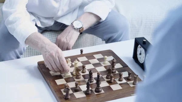 partial view of elderly man playing chess with friend at home