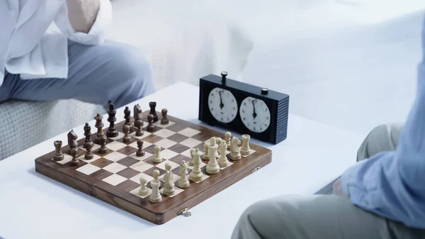 partial view of senior chess players gaming near timer at home