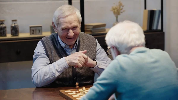 laughing man playing chess with senior friend on blurred foreground