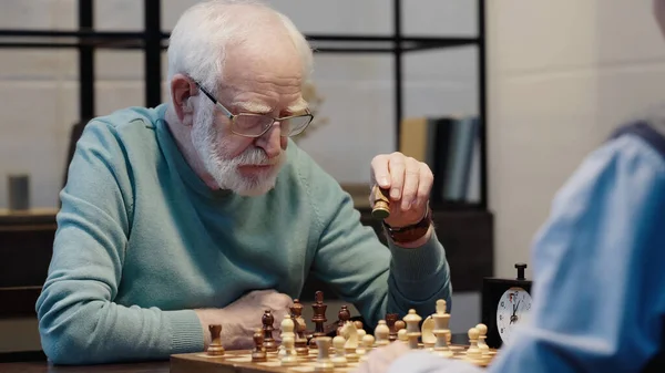 Senior Bearded Man Moving Chess Figure While Gaming Friend Home — Zdjęcie stockowe