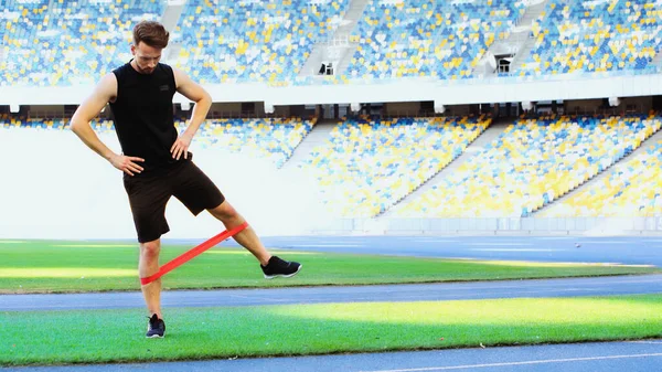Tam boy sakallı sporcu elleri kalçasında direnç bandıyla egzersiz yapıyor.