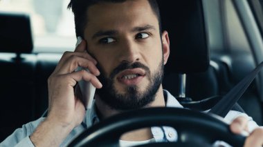 thoughtful bearded man driving auto during conversation on smartphone