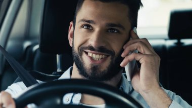 young and happy man driving car while calling on mobile phone