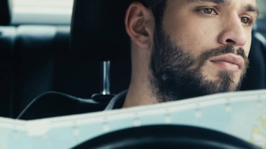 young bearded man holding map while sitting in car